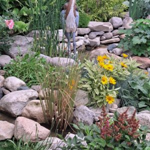 A bird sculpture among rocks and plants in a scenic garden