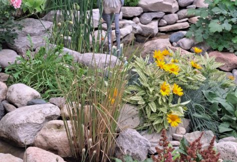A bird sculpture among rocks and plants in a scenic garden